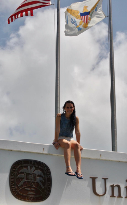 Tiffany Gonzalez sits atop a sign for the University of the Virgin Islands