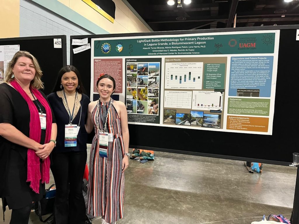 A professor and two students pose next to a scientific poster in an exhibit hall