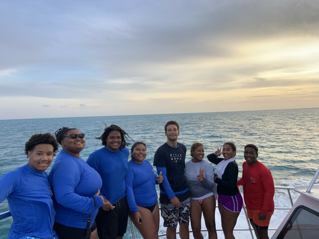 A group of young people pose for a photo on the deck of a boat at sunset